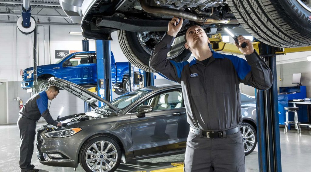 ford shop worker checking the exhaust on a ford on a lift