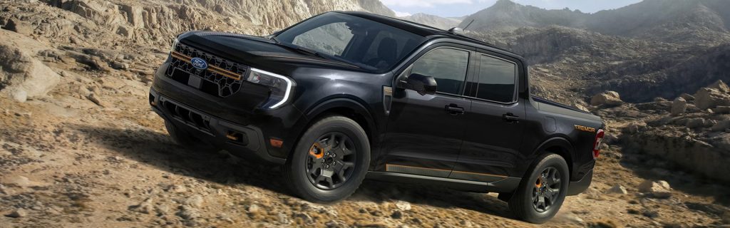 Black pickup truck driving over rugged desert terrain.