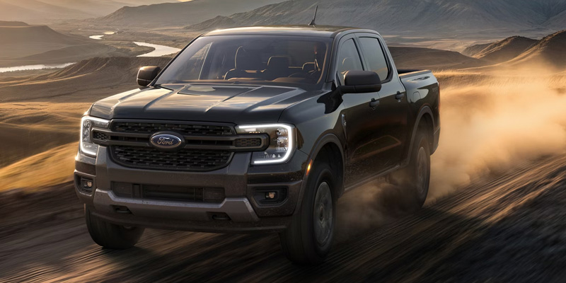 Black Ford Ranger driving on a dirt road through a hilly landscape.