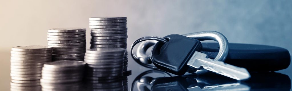 Stacks of coins next to a set of car keys on a reflective surface.