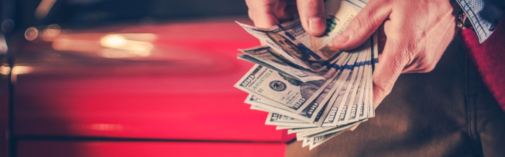 Hands holding cash next to a red car